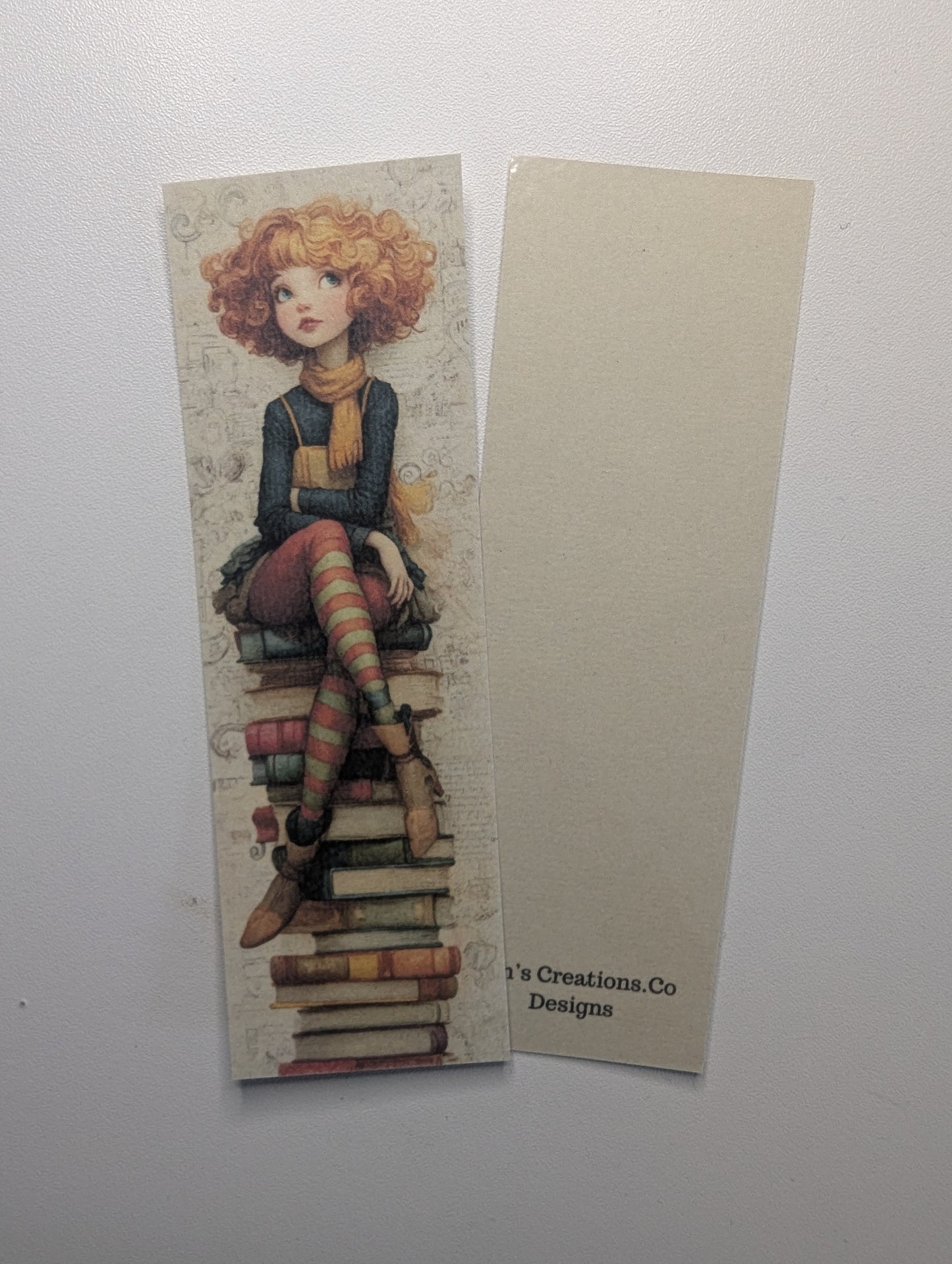 Bookmark with a design of a person with red hair sitting on books, on a white background.