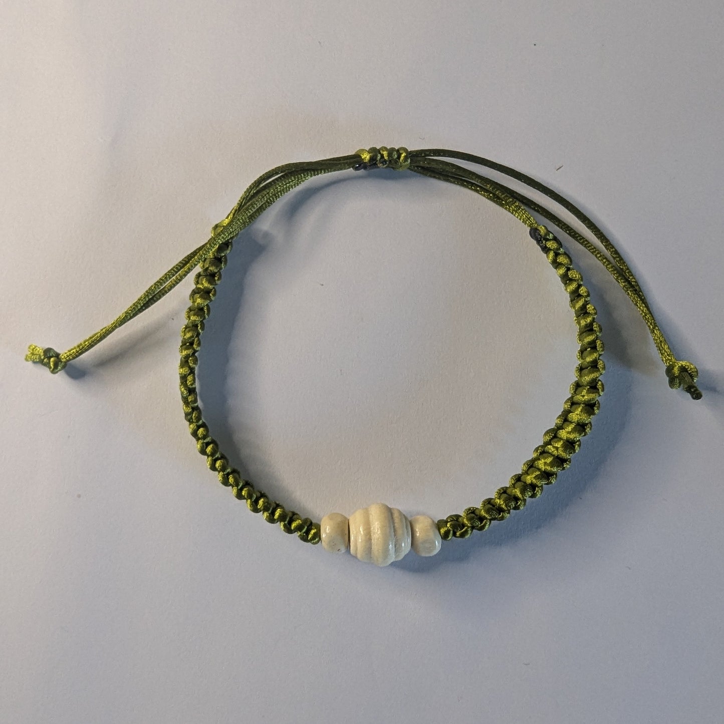 Green braided bracelet with a white bead.
