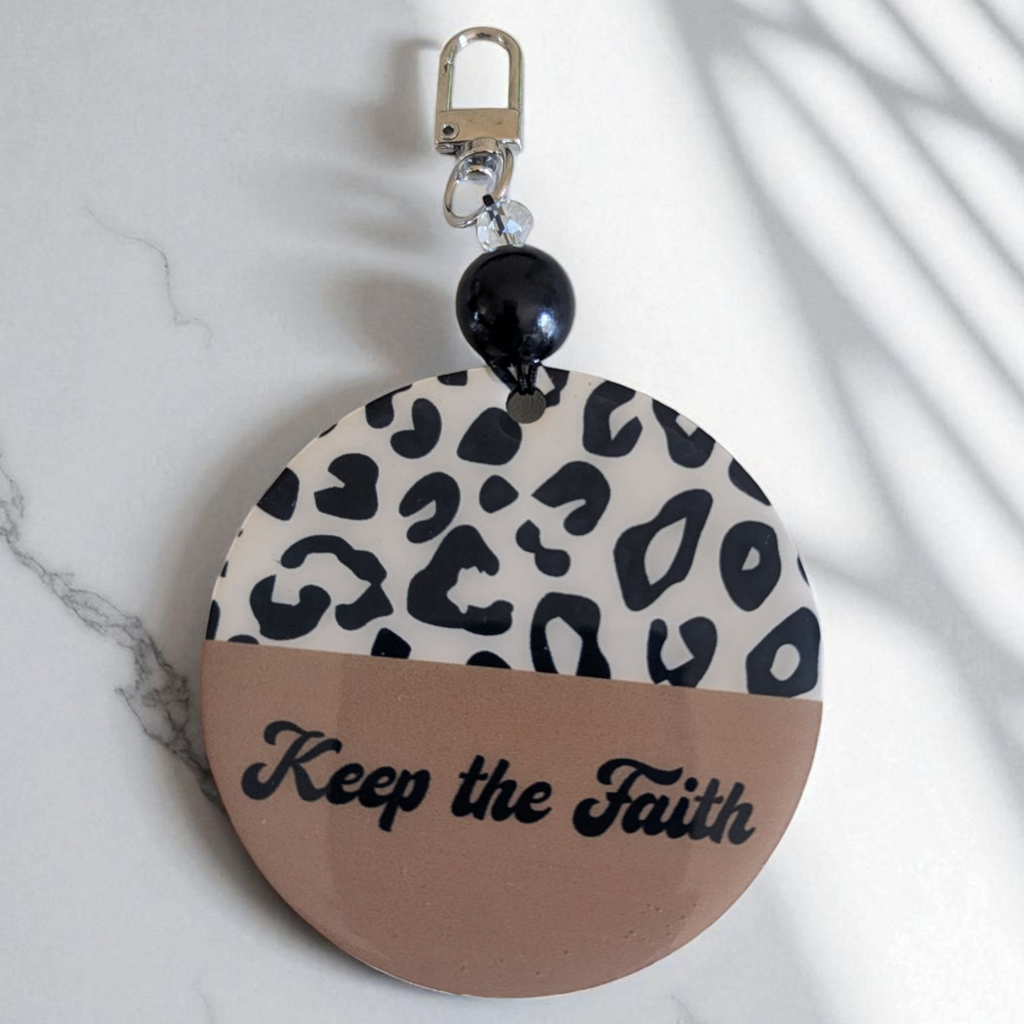 Round keychain with leopard print and 'Keep the Faith' text on a marble background