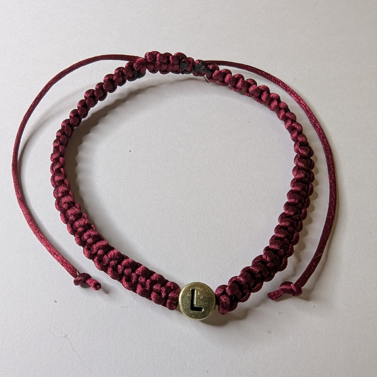 Maroon braided bracelet with a gold charm 