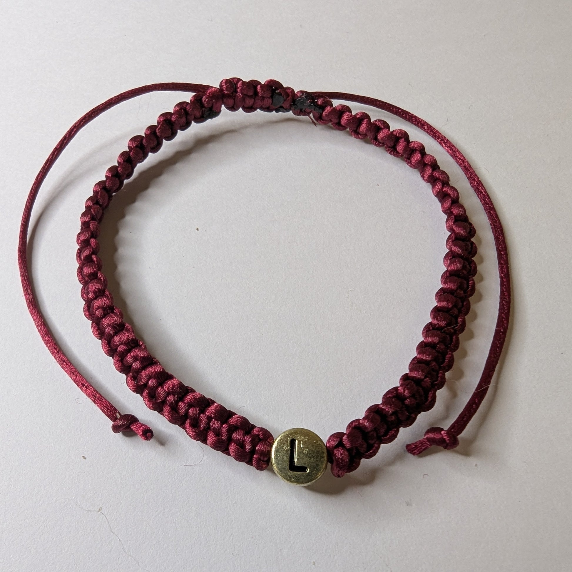 Maroon braided bracelet with a gold charm 