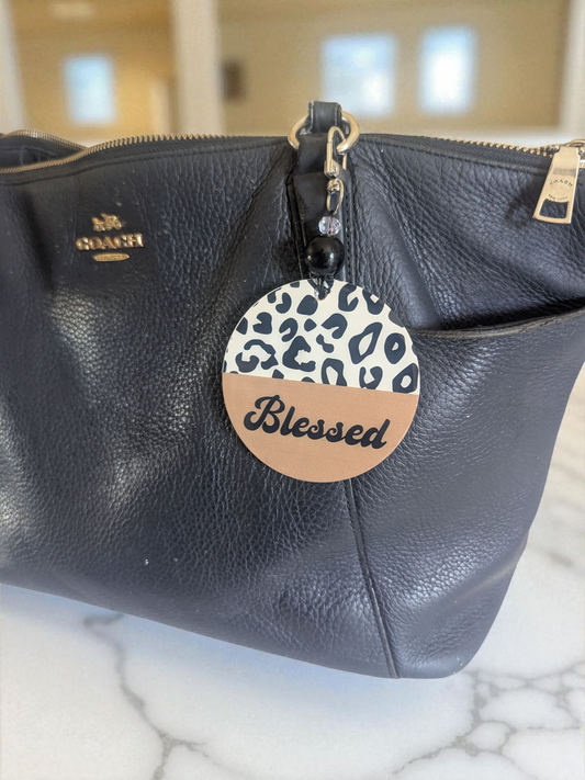 Black leather handbag with a 'Blessed' tag featuring a leopard print design.