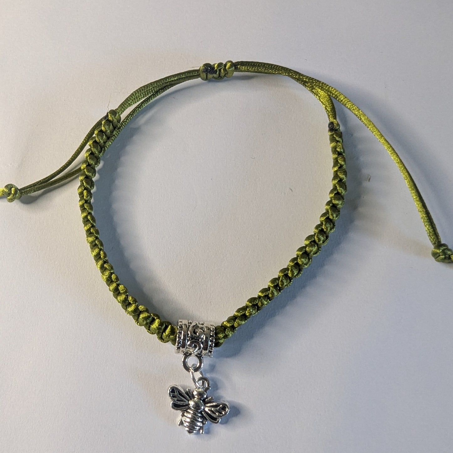 Green bracelet with a silver bee charm.
